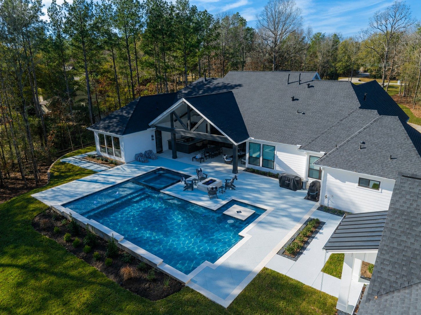 Aerial view of a geometric pool and flush spa beside a modern farmhouse with a black-and-white palette