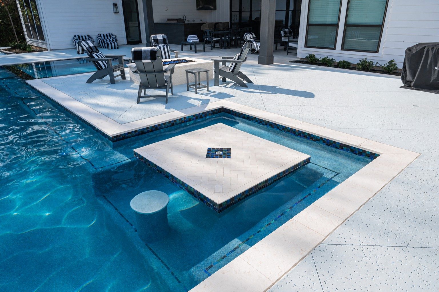 Flush spa with white cap and glass-tile band sitting inside the pool's edge