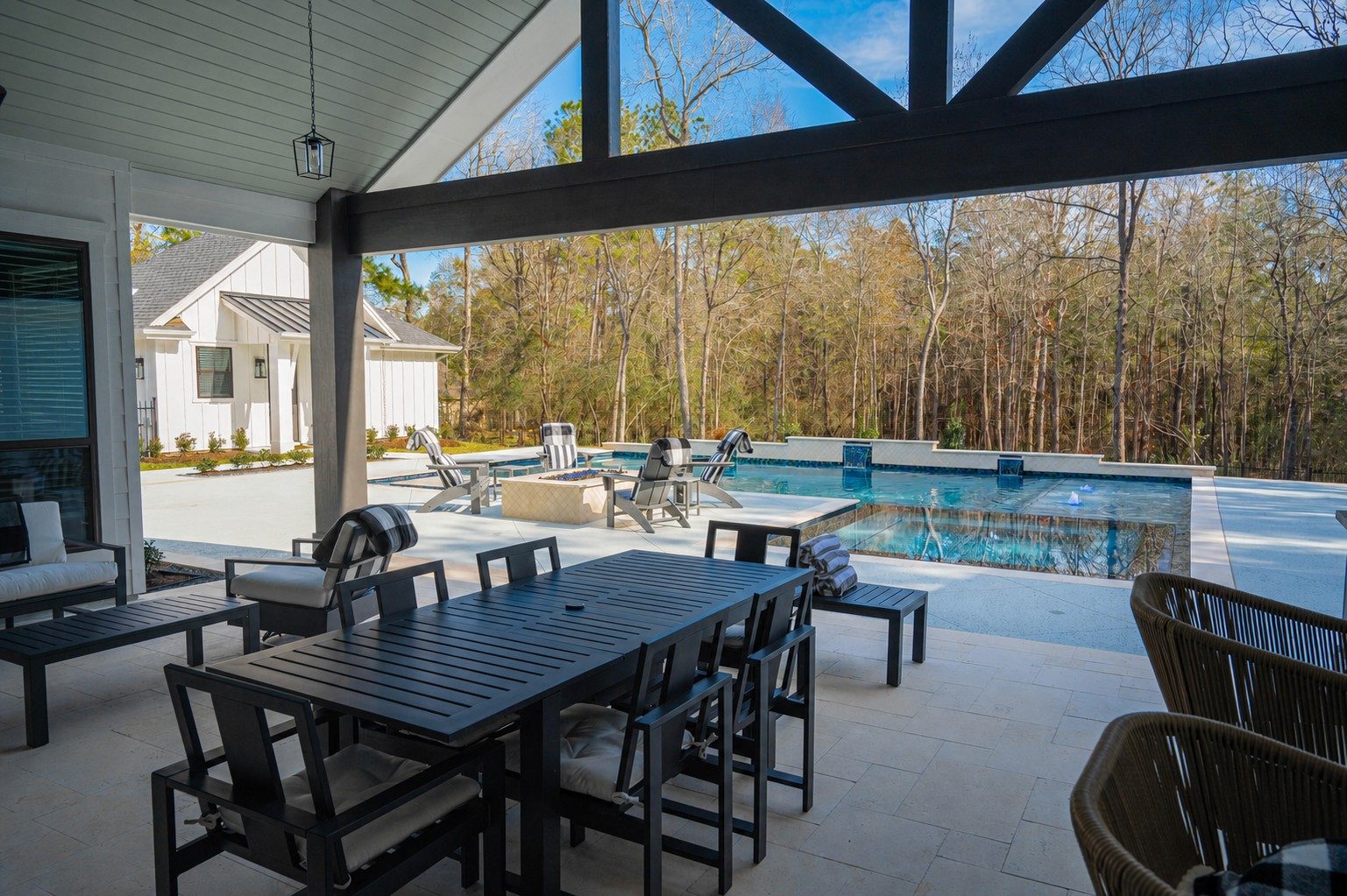 Covered outdoor dining area with black table and chairs looking out over the pool